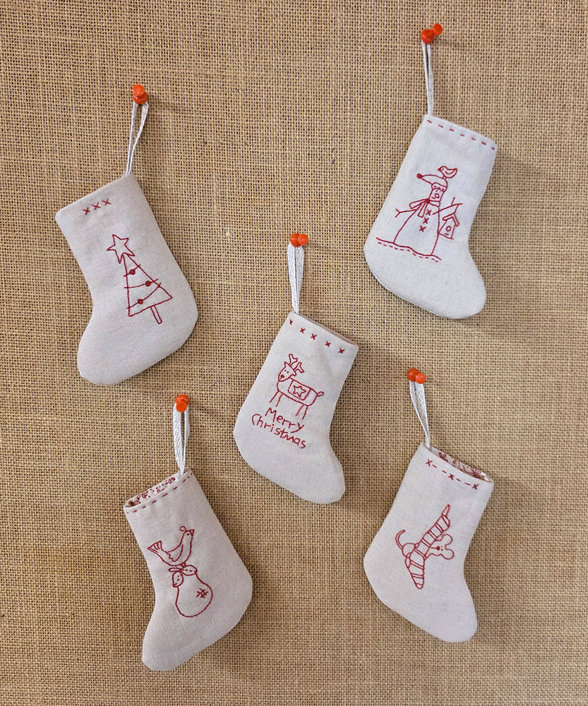 Set of five mini redwork stitchery stockings hanging on Christmas tree