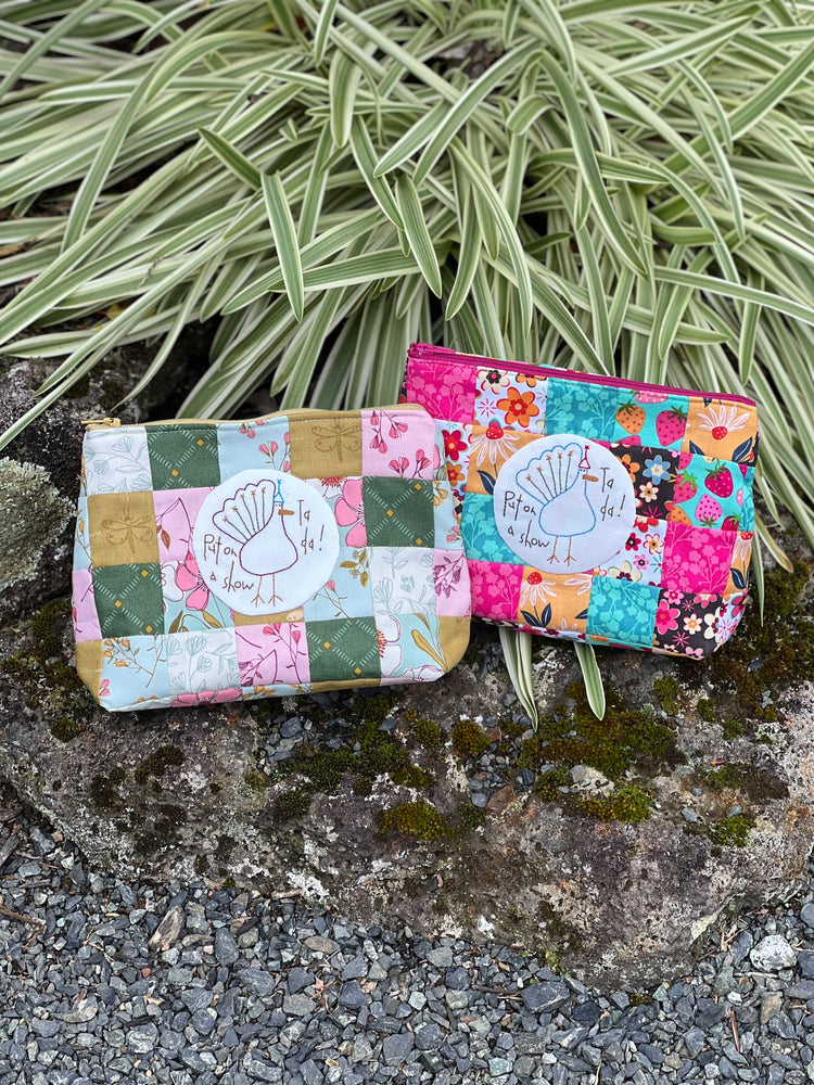 Two patchwork pouches on a rock with green plants in the background