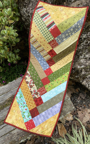 
                  
                    Scrappy Christmas Table Runner with festive quilted patterns.
                  
                