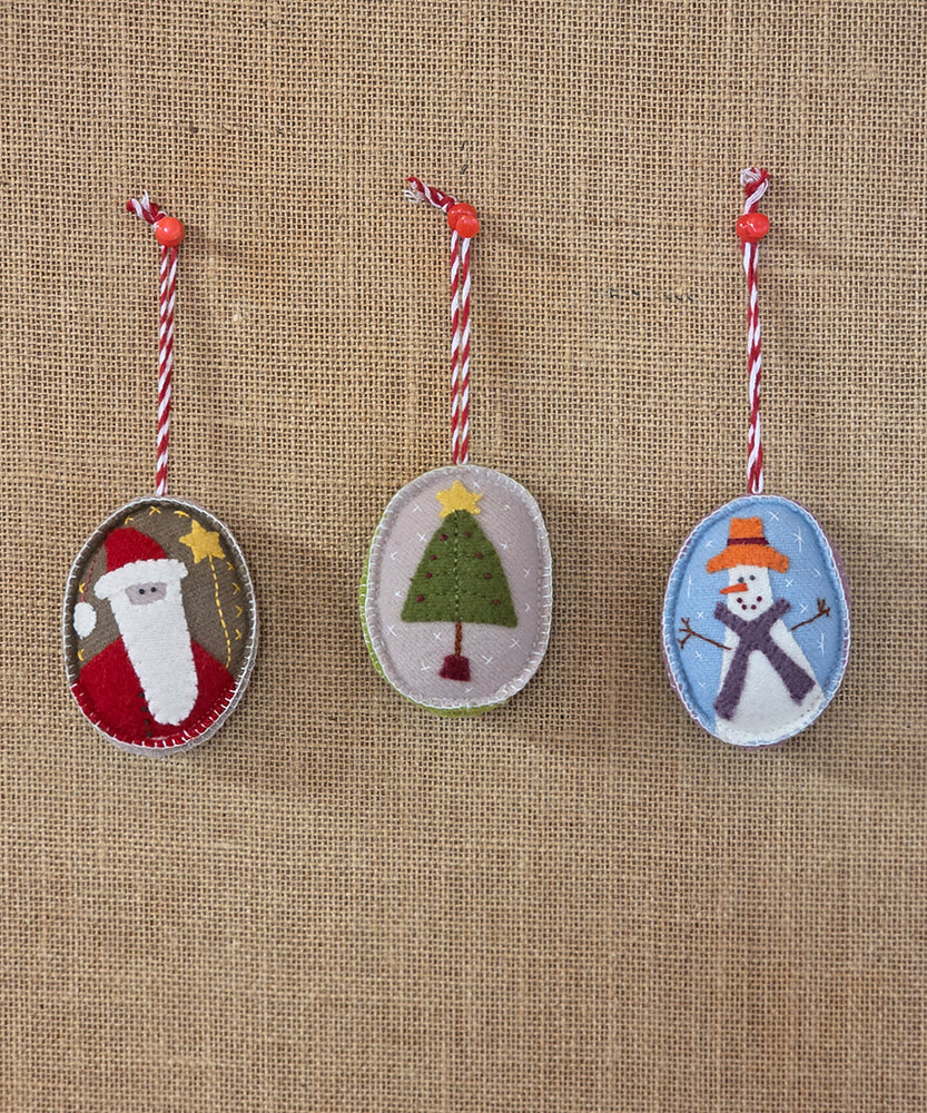 Three felt Christmas ornaments with Santa, a tree, and a snowman on a burlap background.
